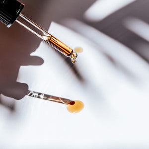 Golden drop of Olive-C60™ Integrative Facial Serum falling from a glass dropper